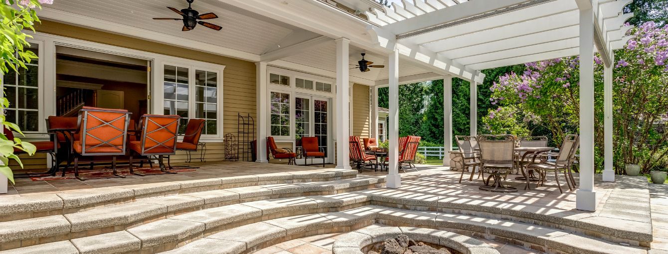 A spacious outdoor patio with a covered pergola featuring white columns and ceiling fans