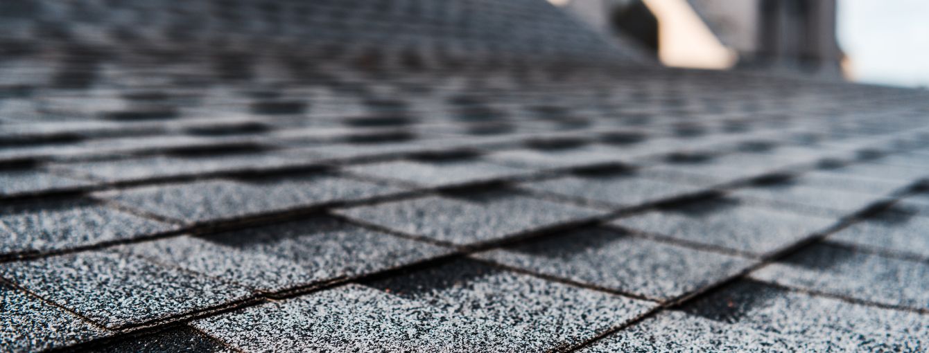 Close-up of asphalt shingles arranged in a staggered pattern on a roof, showing textured surface and layered design.